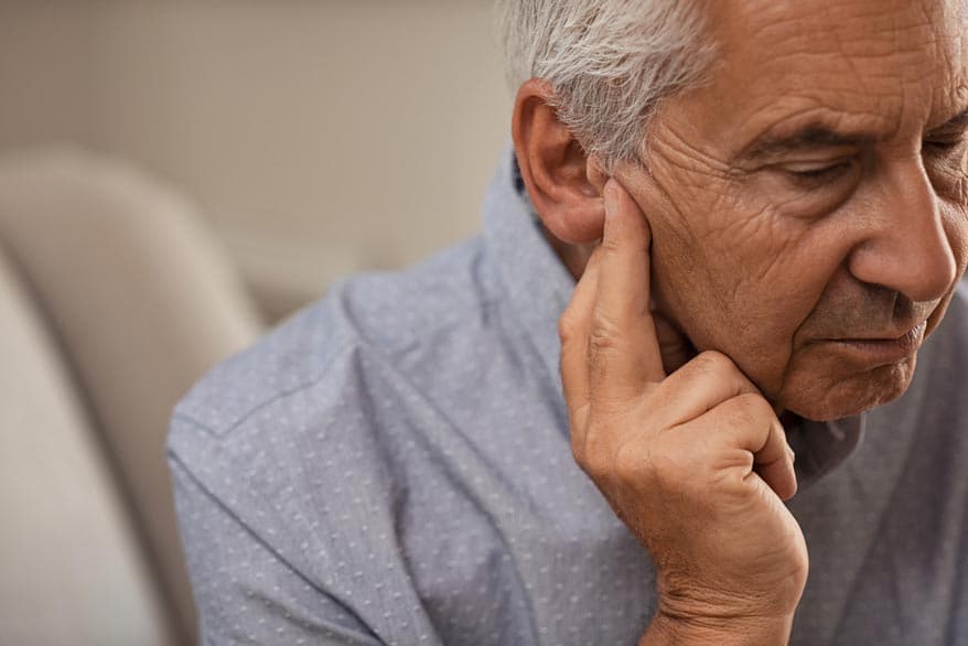 Senior drückt mit seinen Finger am Ohr