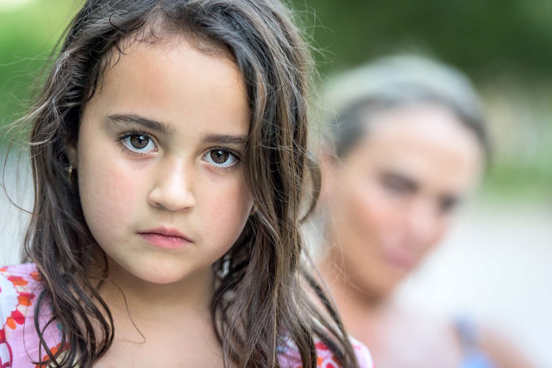Draußen Bild eines sechs Jahre alten kleinen Mädchens des seriösen Latino, das mit ihrer Mutter im Hintergrund aufwirft