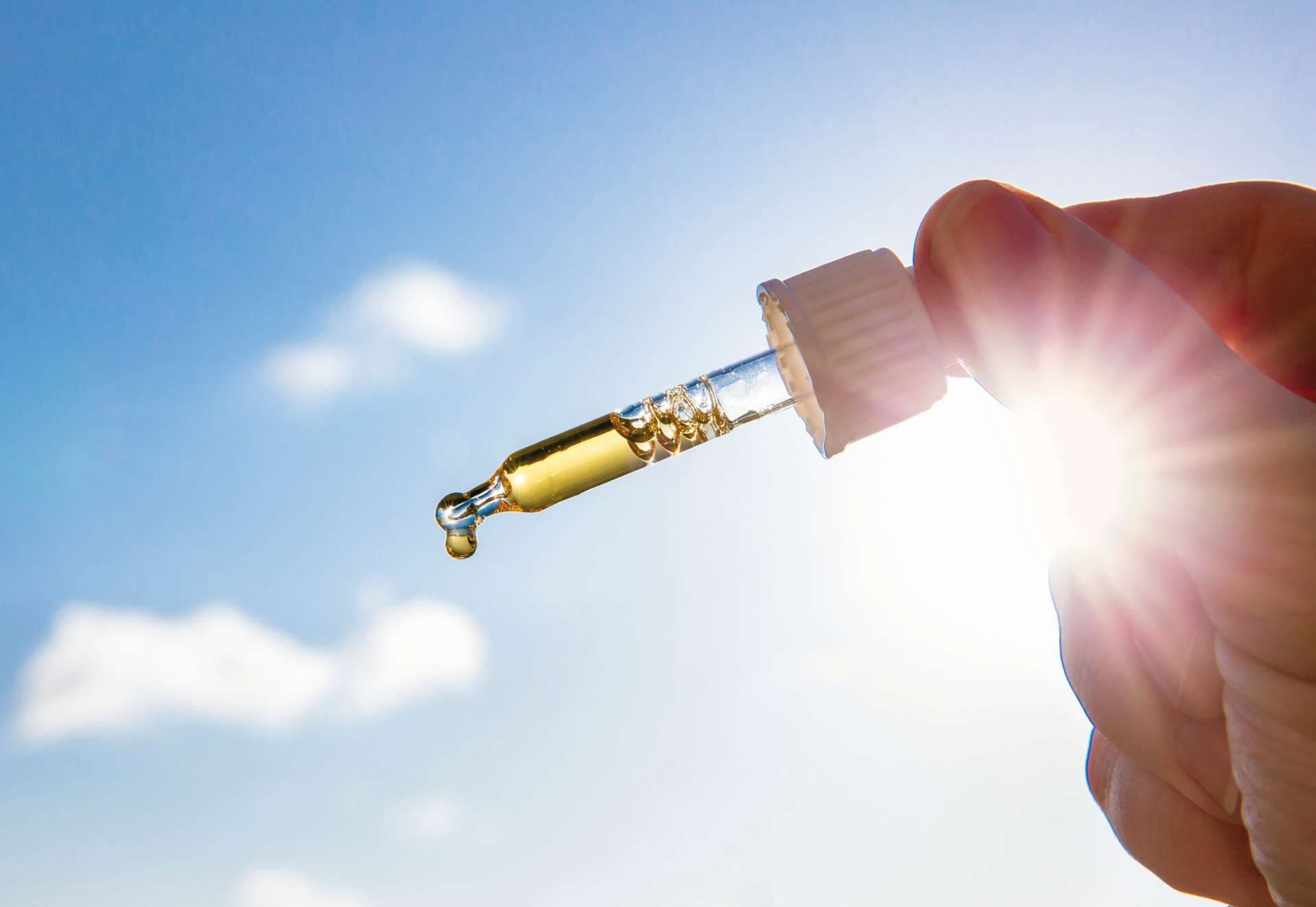 Hand, die Pipette mit schönem goldenem flüssigem D-Vitamin gegen Sonne und blauen Himmel am sonnigen Tag hält. Vitamin D hält Sie gesund, während es im Winter an Sonne mangelt.