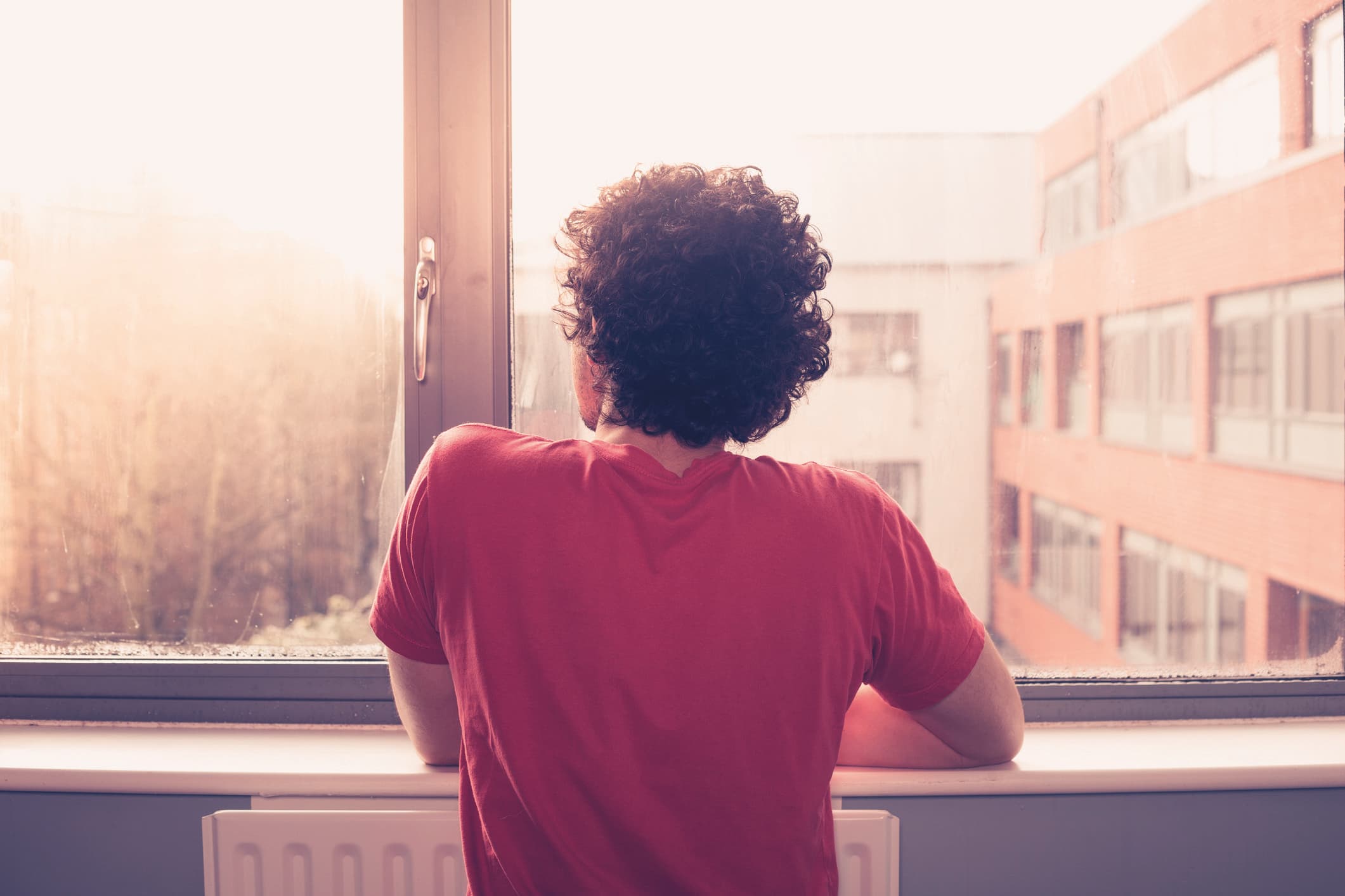 Junger Mann ist am Fensterbrett und schaut auf Sonnenuntergang hinaus