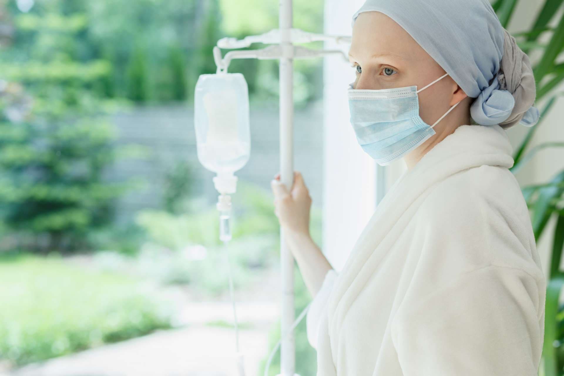 Junge Frau mit Tropf, der durch das Krankenhausfenster steht