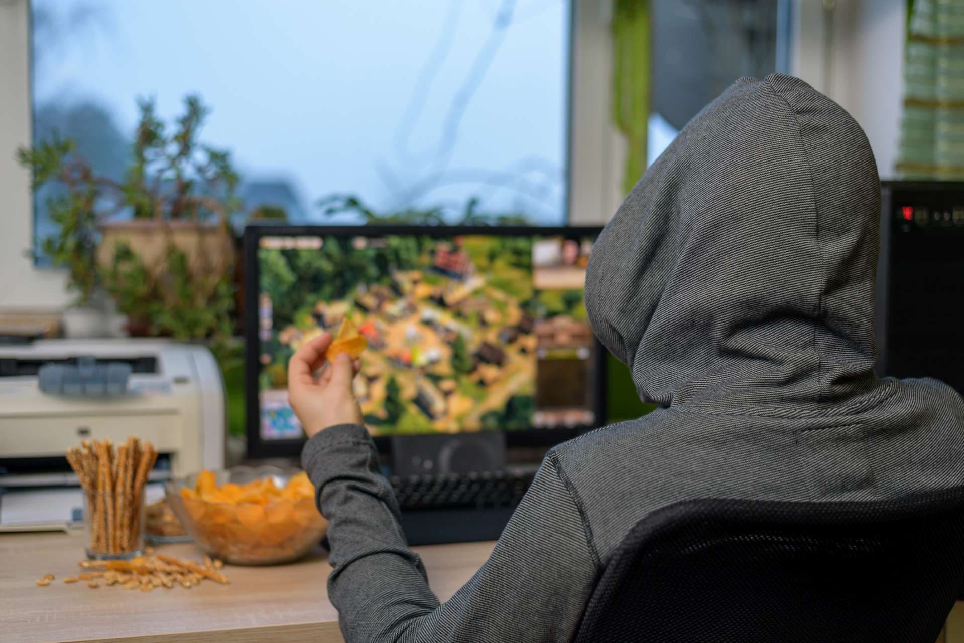 männlicher Spieler, der Strategiespiel auf Computer spielt, der Snacks isst