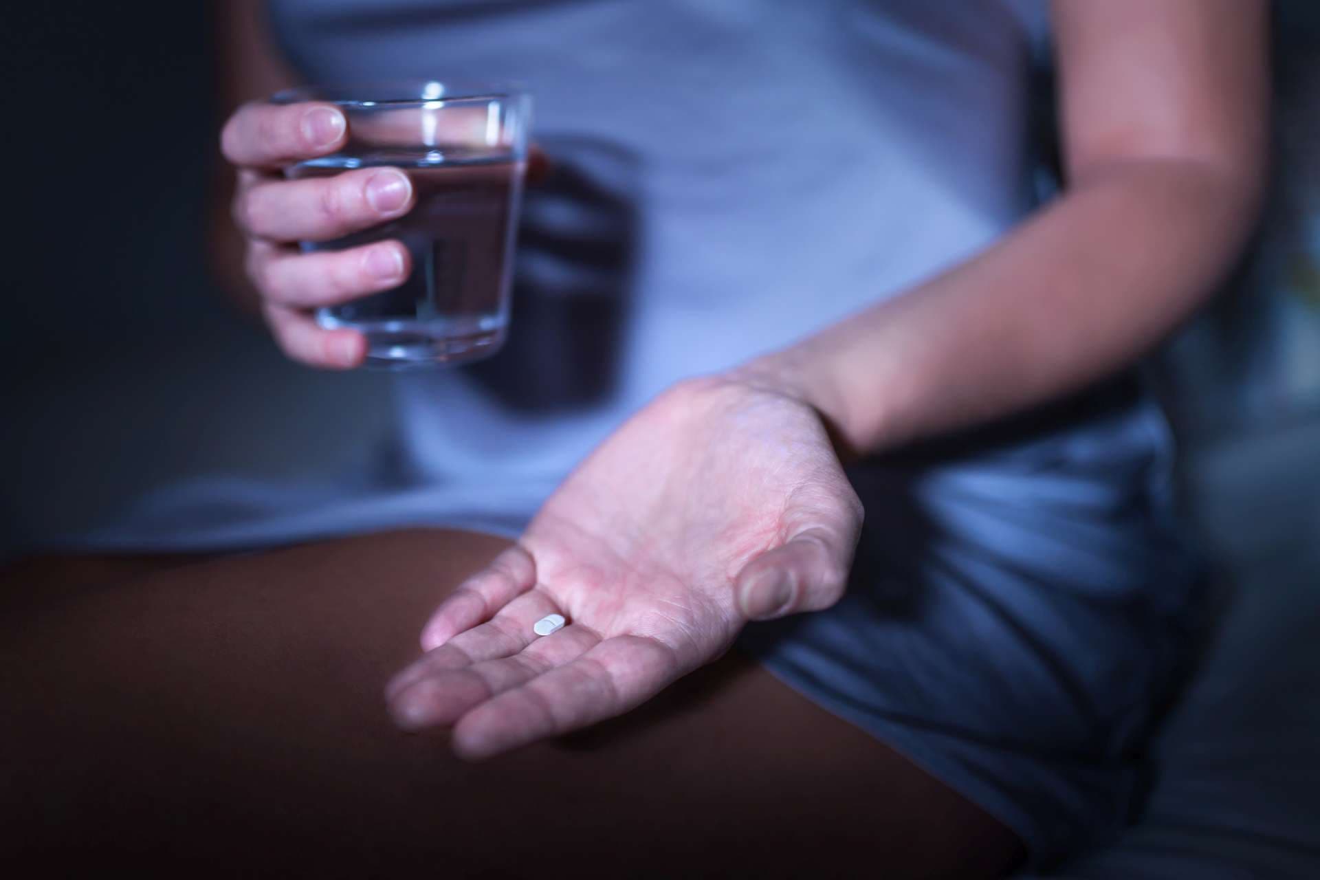 Schlaftablette in der Hand. Frau, die auf Bett mit Medizin für Schlaflosigkeit oder Melatonin sitzt. Schlaflose und müde Frau kann nicht einschlafen. Medizinische Pille und Tablette gegen Kopfschmerzen oder Migräne.