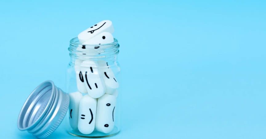 Pills with funny faces and a glass bottle on a blue background. Pharmacy antibiotic. Treating with antidepressant. Mental disorder. The concept of antidepressants and healing. Copy space.