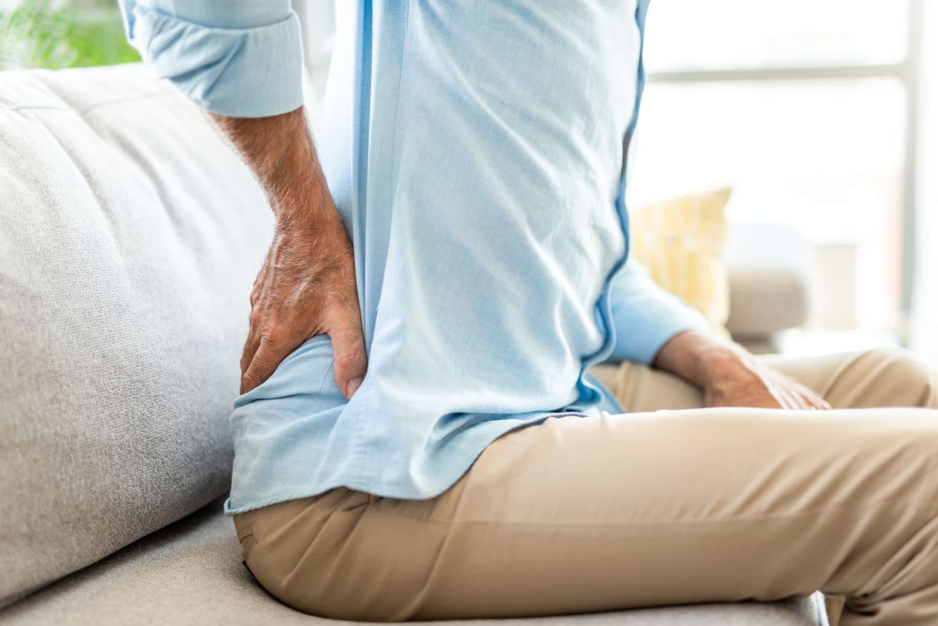 Close-up of unrecognizable senior man having back pain while sitting in the living room.