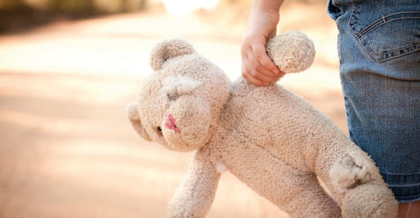 Farbiges Foto auf Lager eines kleinen außer Kontrolle geratenen Mädchens, das einen alten Teddybär an der Seite einer unbefestigten Straße im ländlichen Land hält.