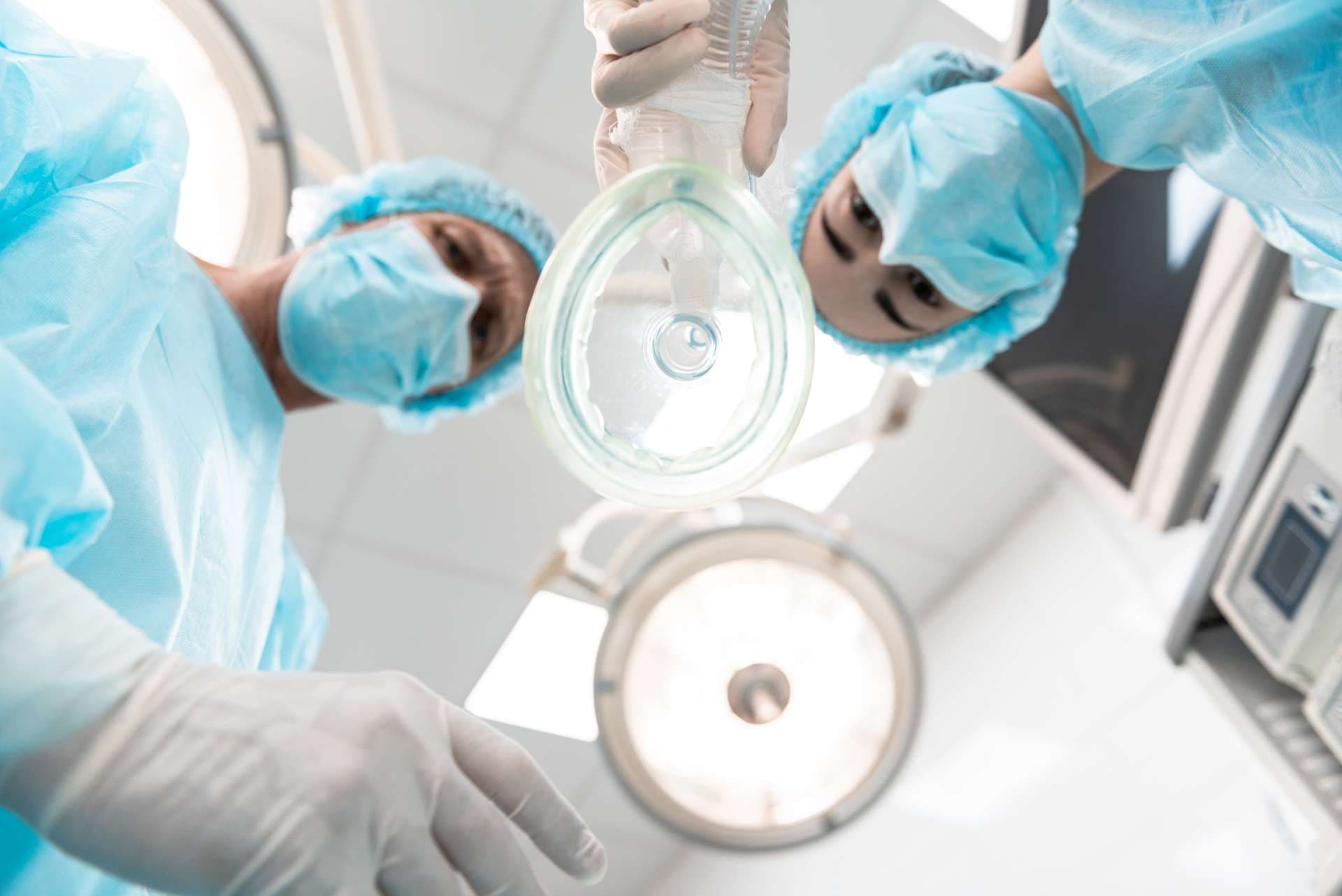Zwei ernsthafte Ärzte, die blaue Masken tragen und Sie im Stehen mit der Narkosemaske ansehen