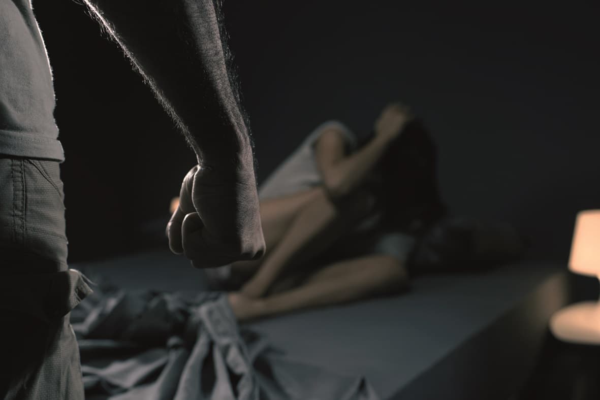 Mann bedroht eine Frau im Schlafzimmer, sie hat Angst und liegt im Bett, häusliche Gewalt Konzept