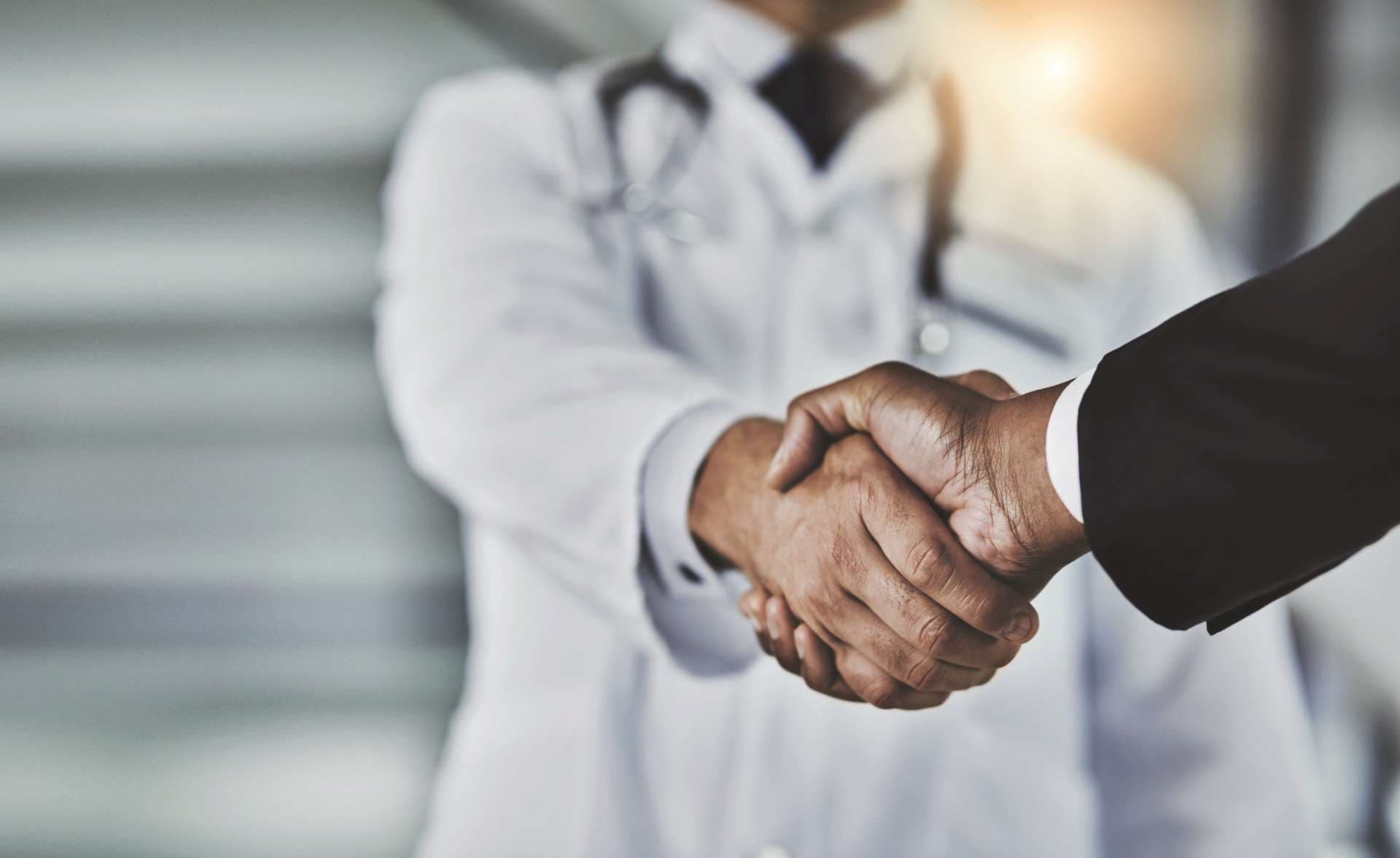 Kurzer Schuss eines Arztes, der einem Geschäftsmann in einem Krankenhaus die Hand schüttelt