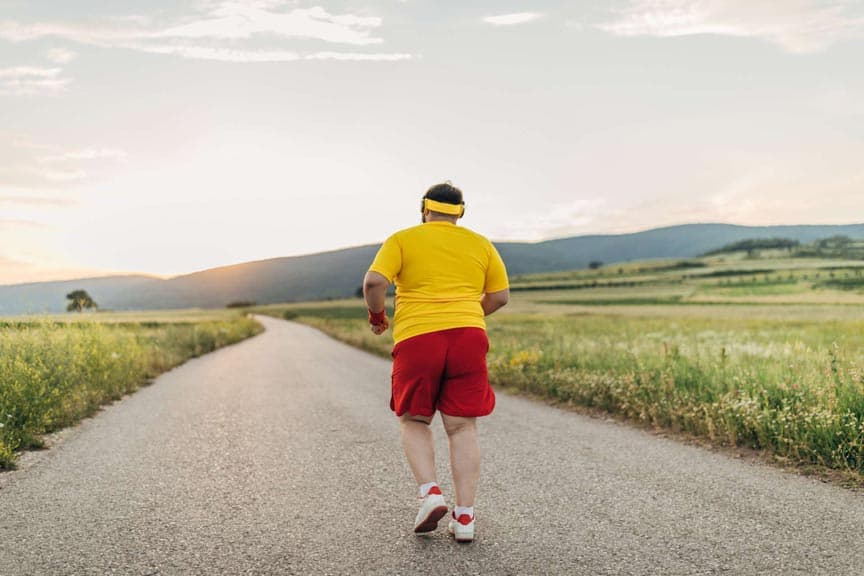 Ein übergewichtiger Mann, der allein auf der Straße joggt, Musik über Kopfhörer hört, Rückansicht.