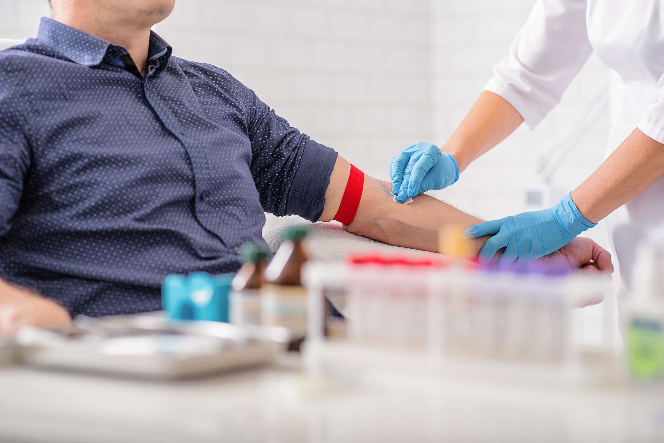 Nahaufnahme einer Krankenschwester, die den männlichen Arm vor dem Bluttest desinfiziert. Mann sitzt auf einem Stuhl in der Nähe des medizinischen Sets