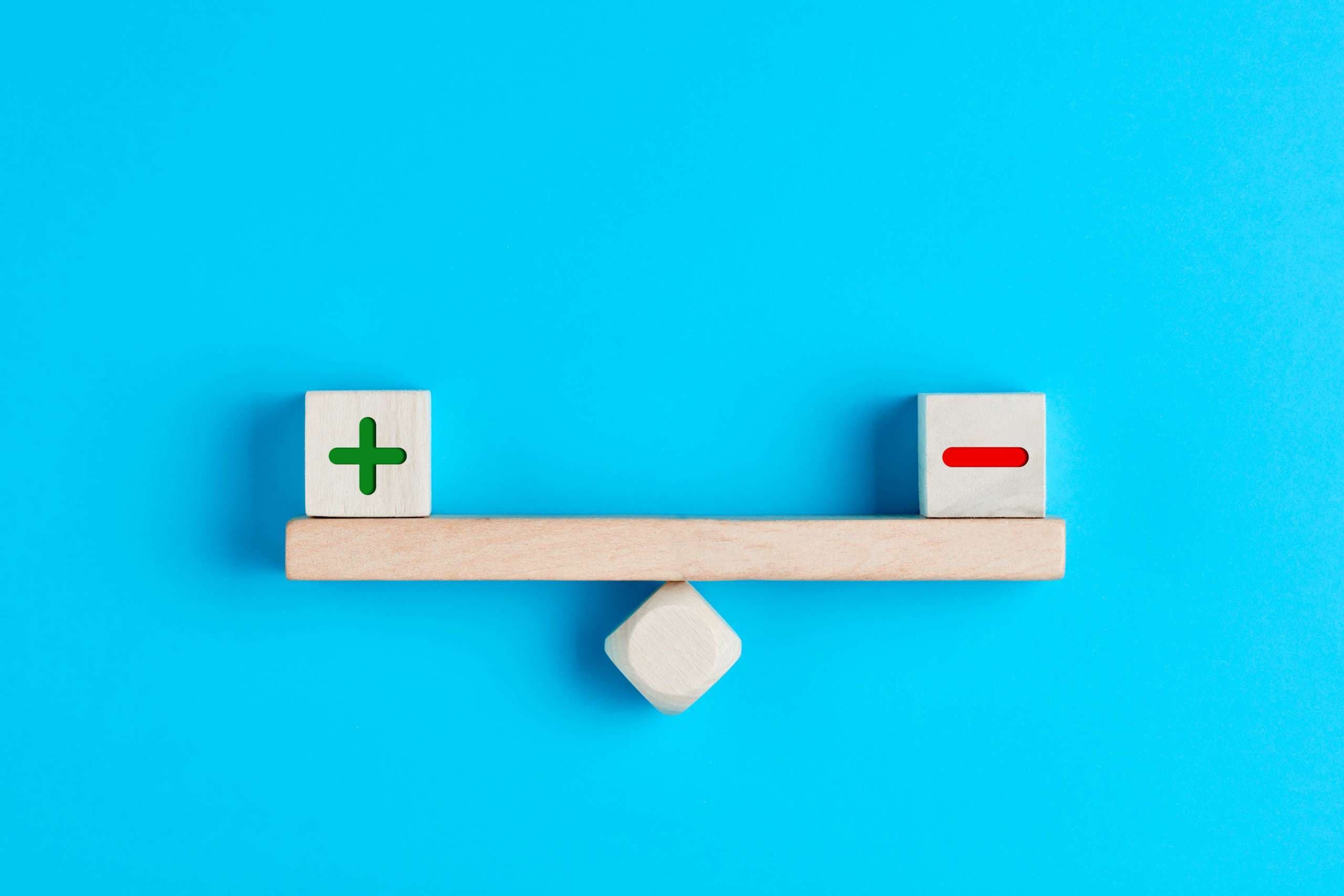 Plus und Minus oder positive und negative Symbole auf Holzklötzen sind auf einer Holzwippe im Gleichgewicht