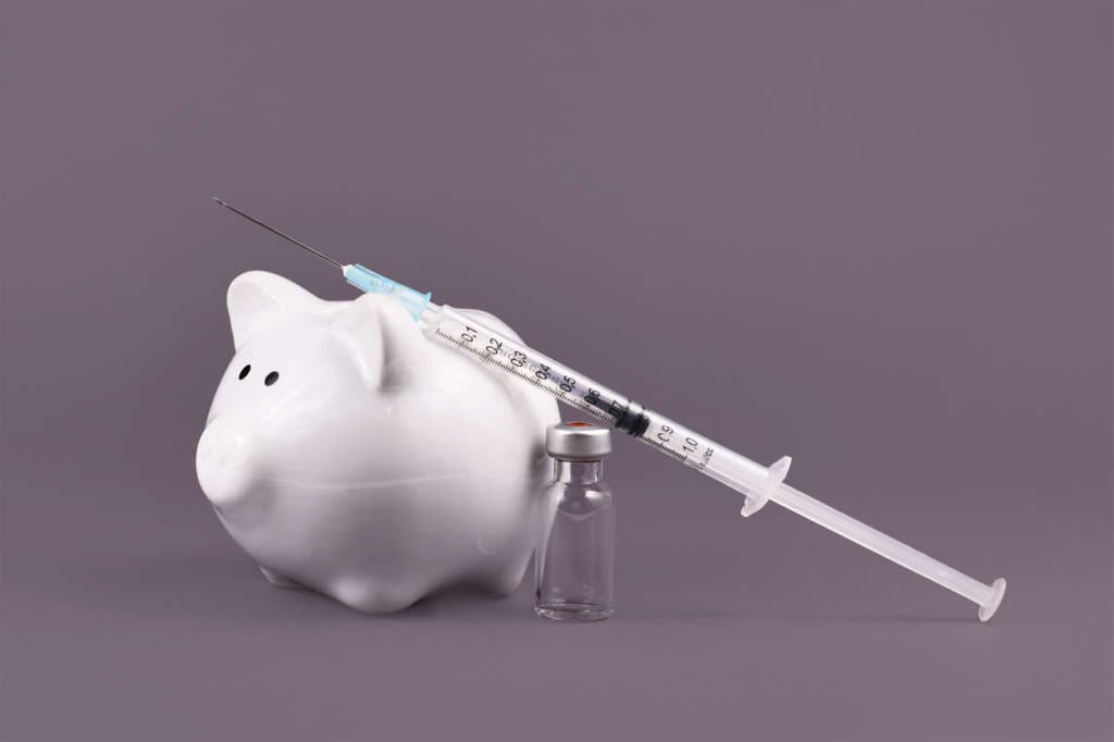 Corona virus vaccination costs concept with syringe, vaccine vial and piggy bank on gray background
