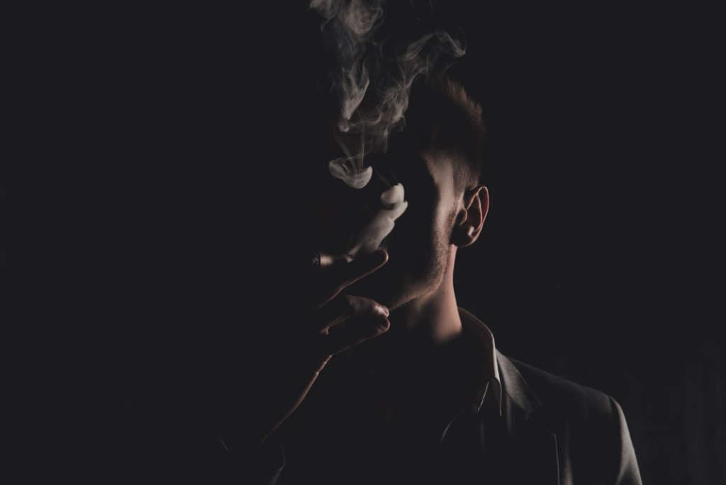 Mystery man with cigar and smoke isolated on black background