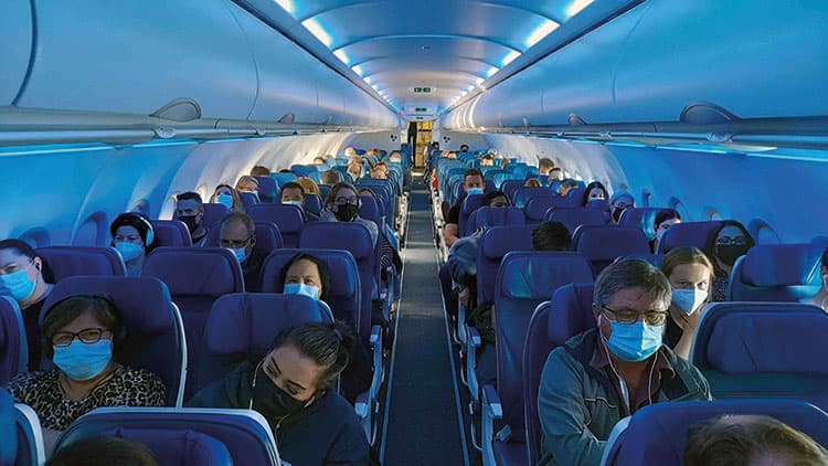 Gang eines vollen Flugzeuges mit Passagieren, die eine Gesichtsmaske tragen