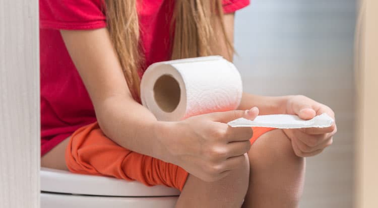 A child is sitting on the toilet and holding toilet paper in his hands