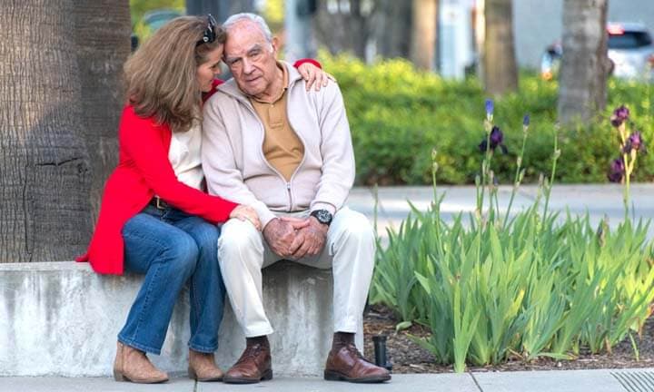 senior Hispanic or middle Eastern man possing with his mature caucasian daughter in the street, she is comforting him