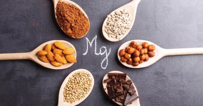 Produkte reich an Magnesium auf Holzlöffeln auf schwarzem Steinhintergrund.