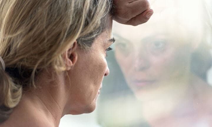 Pensive hispanic mature woman looking through a window