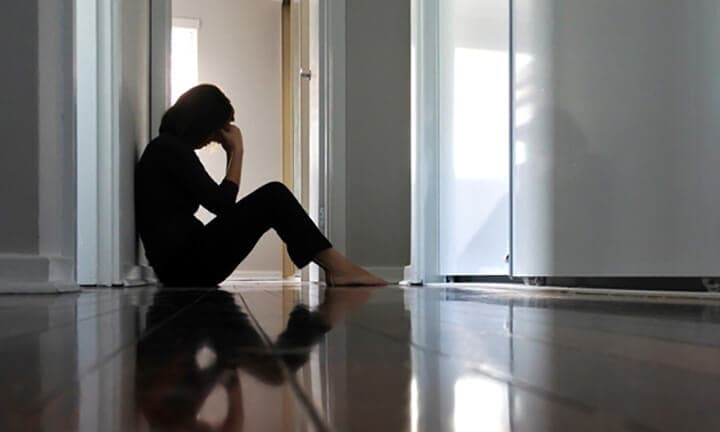 Sad adult woman sitting on dark home corridor floor.