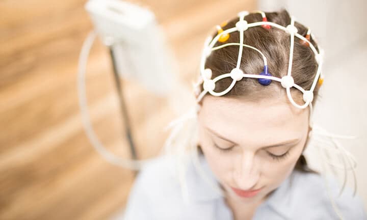 Junge Frau mit Elektrodenausrüstung auf dem Kopf mit klinischem Test im Krankenhaus