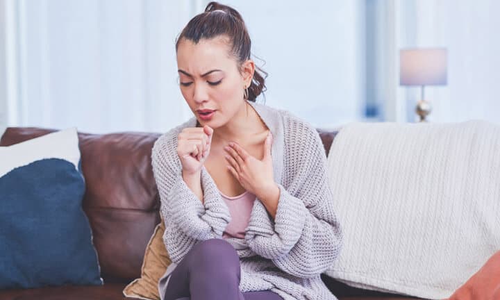 Schnappschuss einer attraktiven jungen Frau, die allein zu Hause auf ihrem Sofa sitzt und hustet