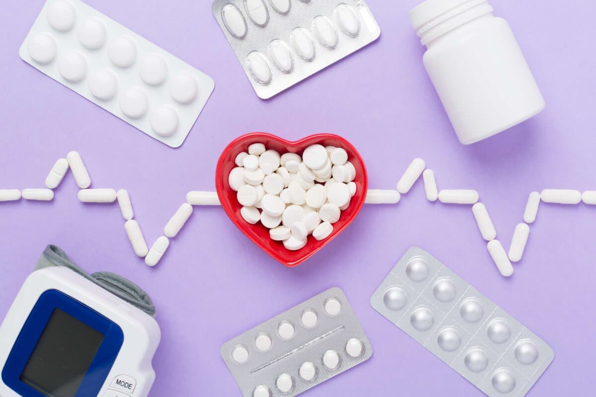 Cardiogram made with medicines and heart-shaped bowl on color background, top view