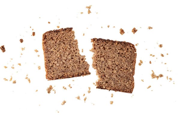 Ein auseinandergerissenes Stück dunkles Brot vor weissem Hintergrund