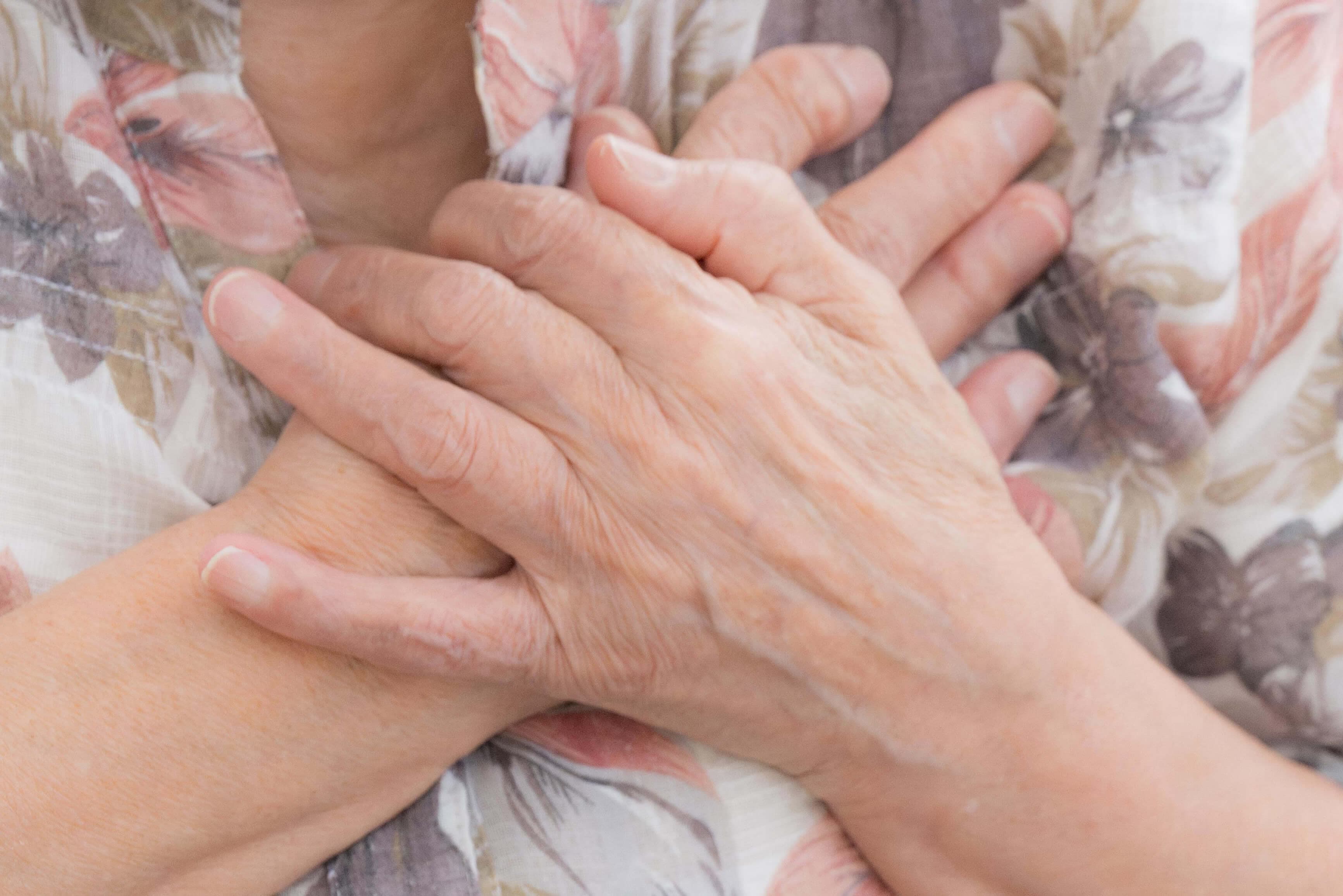 Ein alte Frau faltet ihre Hände vor der Brust.