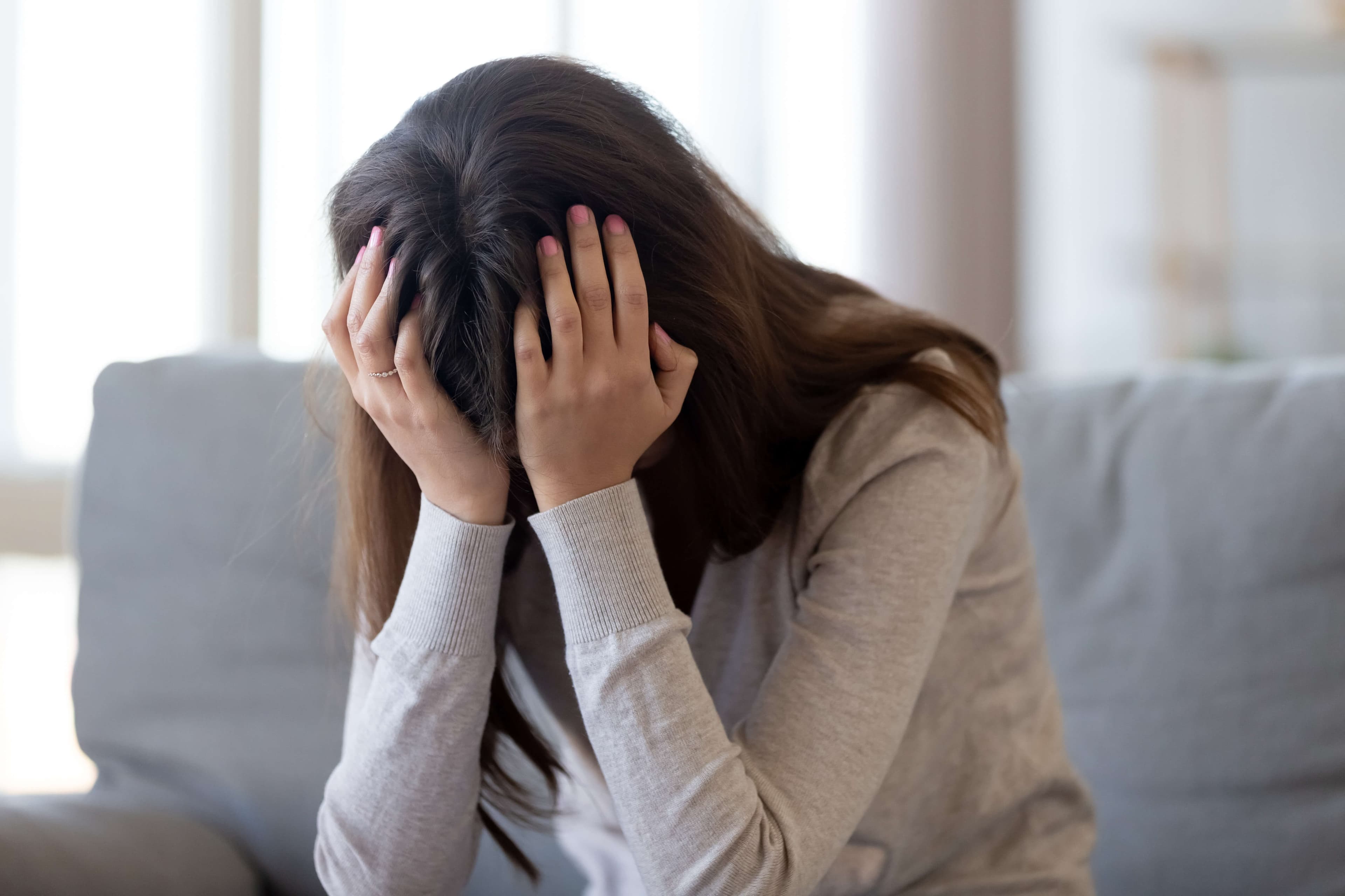 Depressive junge Frau hält Kopf in Händen und fühlt sich verletzt und verärgert