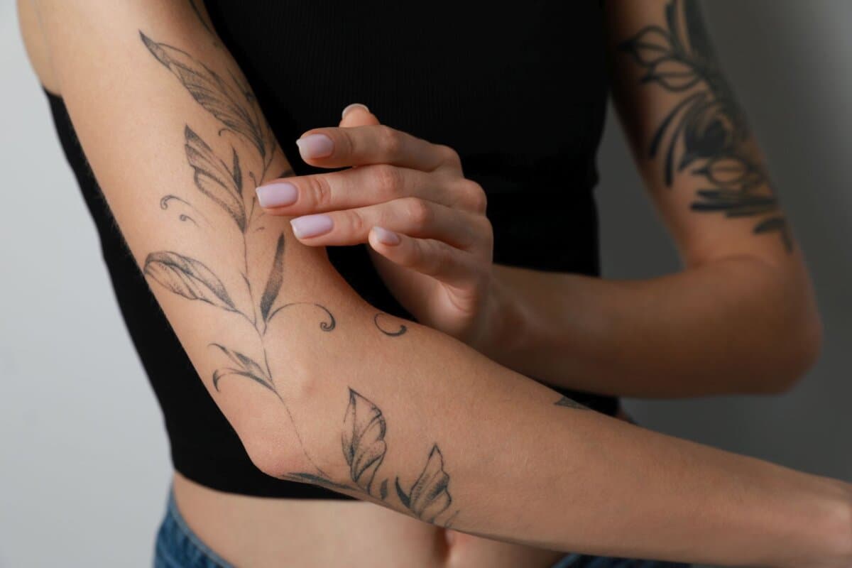 Femme appliquant de la crème sur son bras tatoué sur fond clair, gros plan