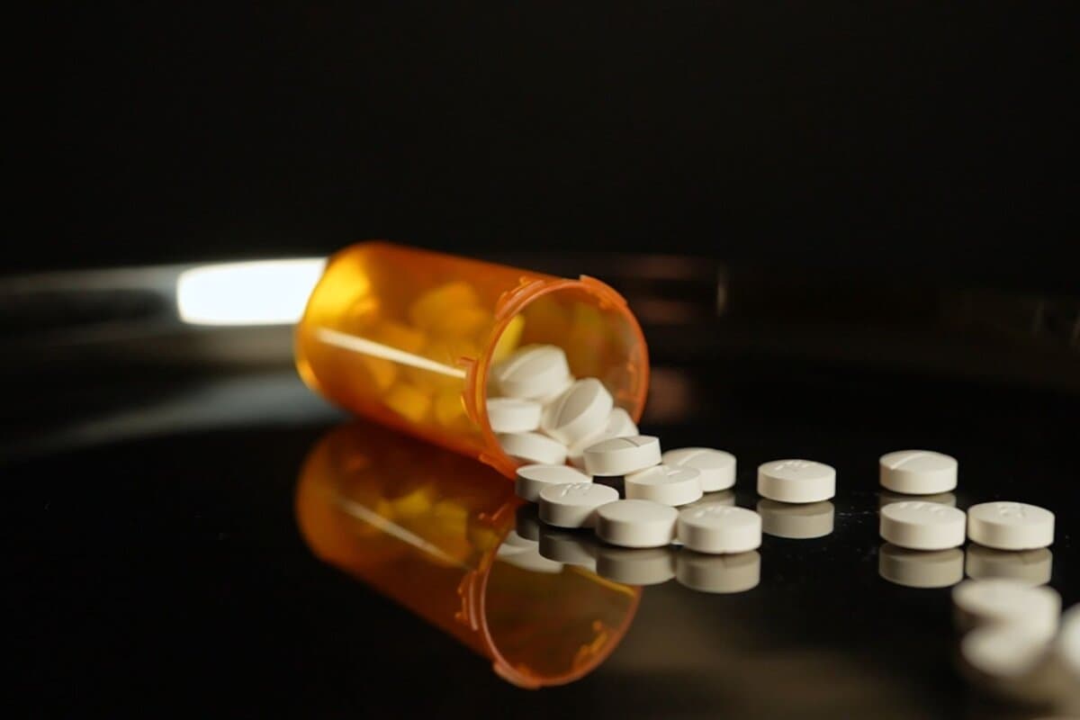 Eine verschreibungspflichtige Pillenflasche steht auf dem Tisch, verstreute Medikamente.