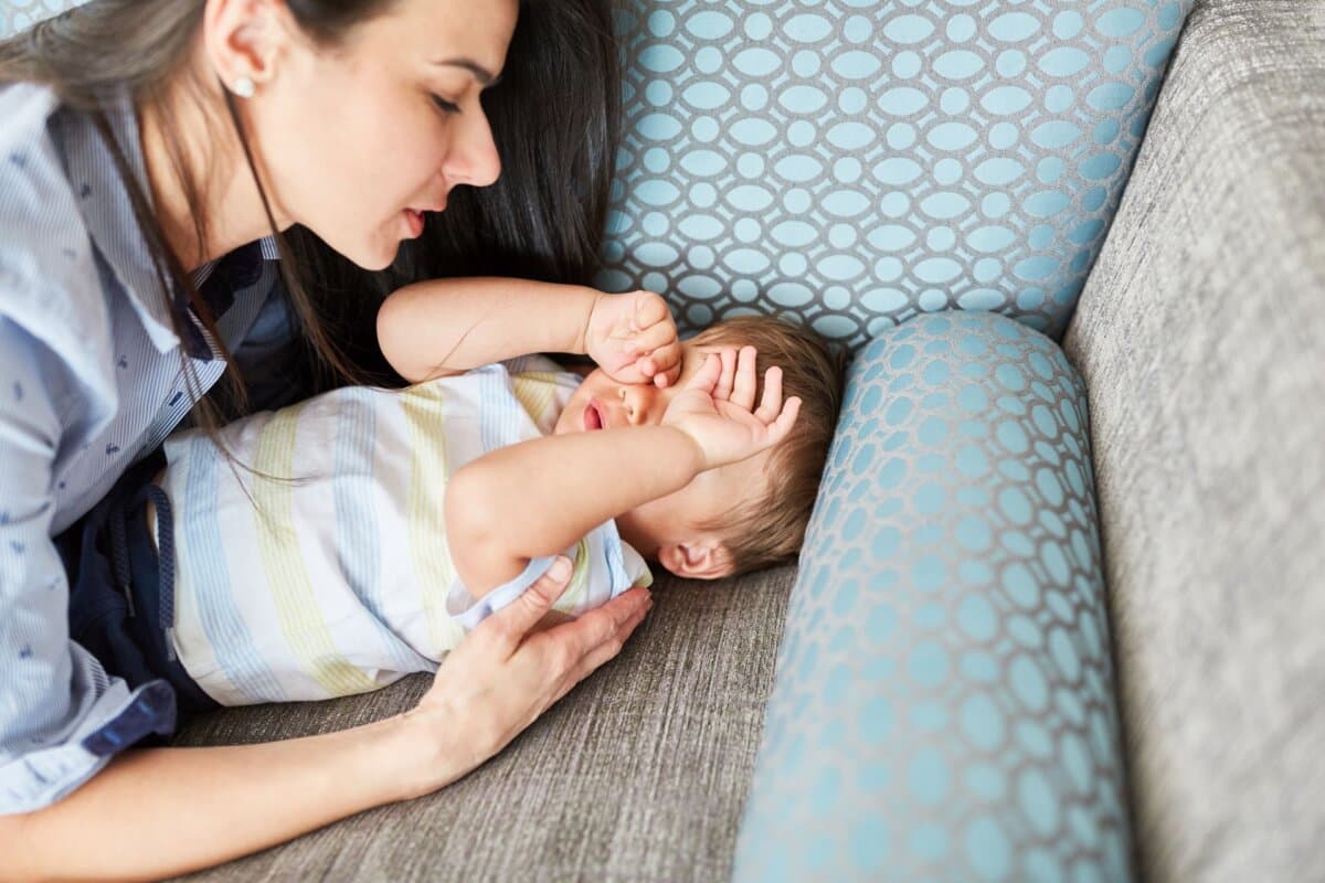 Mutter kümmert sich liebevoll um müdes Kind auf dem Sofa im Wohnzimmer