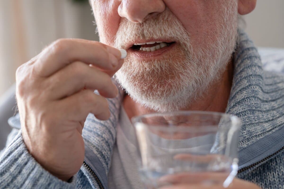 Ein älterer Mann nimmt ein Medikament mit einem Glas Wasser ein