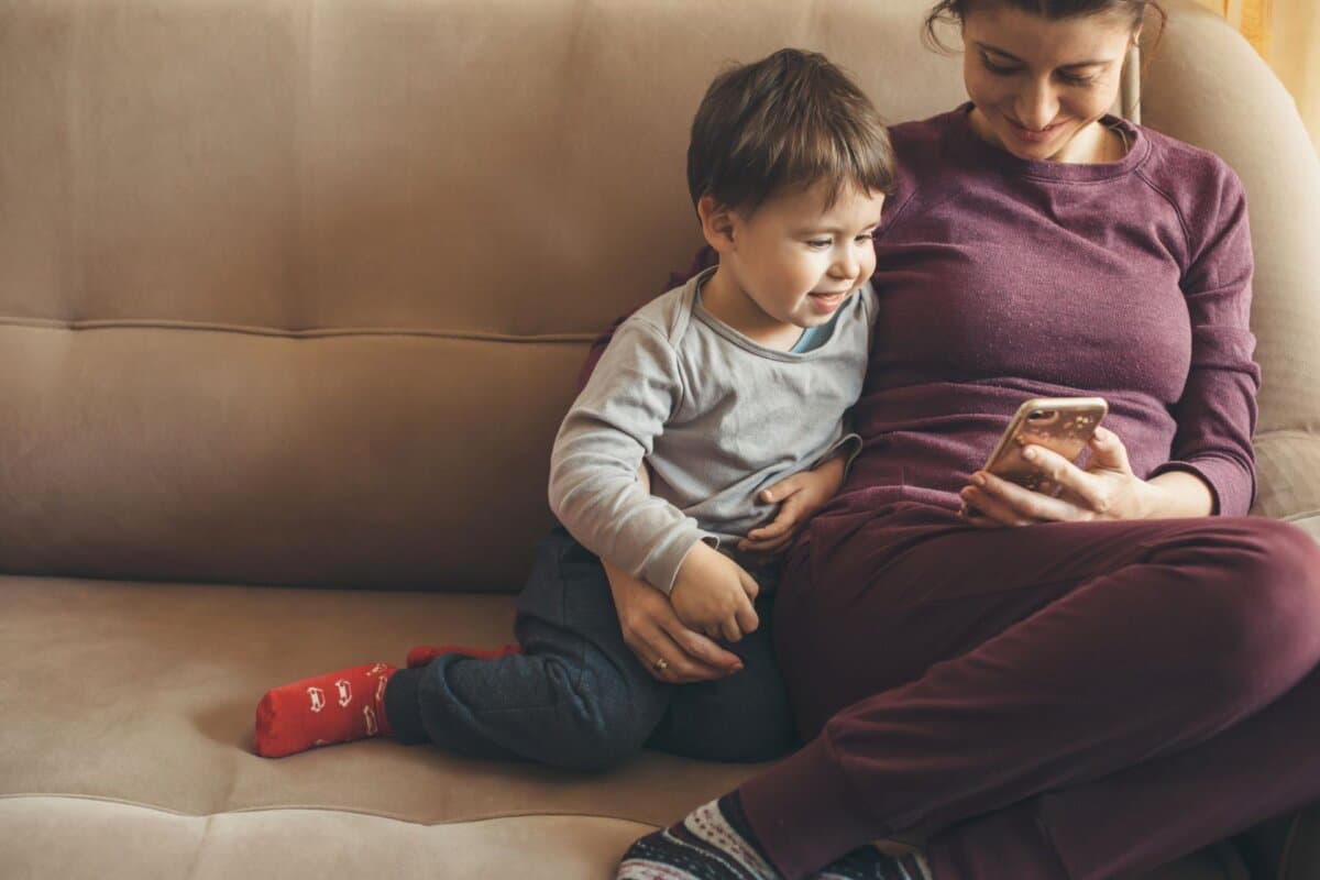 Mutter und Sohn liegen gemeinsam auf dem Sofa und schauen auf ein Smartphone