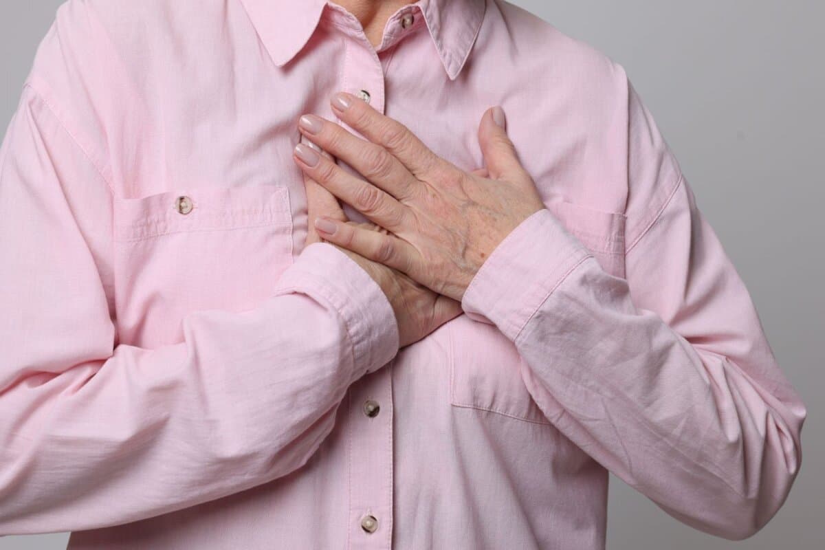 Seniorin mit Brustschmerzen – Nahaufnahme vor grauem Hintergrund, Hinweis auf Herzinfarkt.