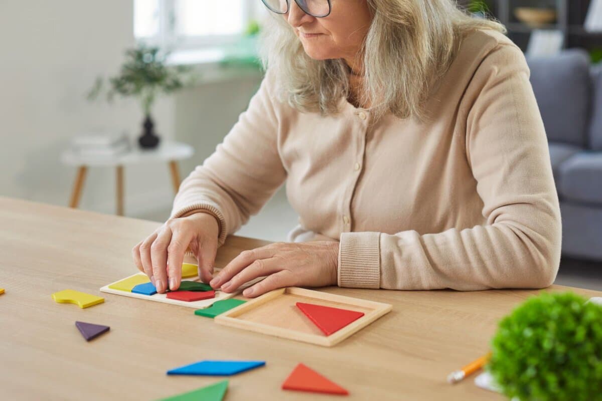 Ältere Frau beim Lösen eines Tangram-Puzzles: Kognitive Fähigkeiten im Fokus.