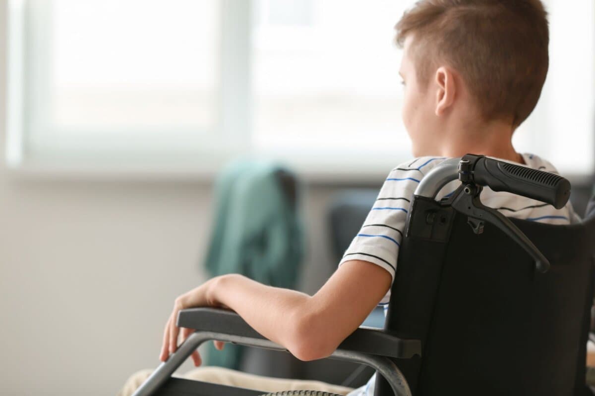 Junge mit neuromuskulärer Erkrankung im Rollstuhl zu Hause.