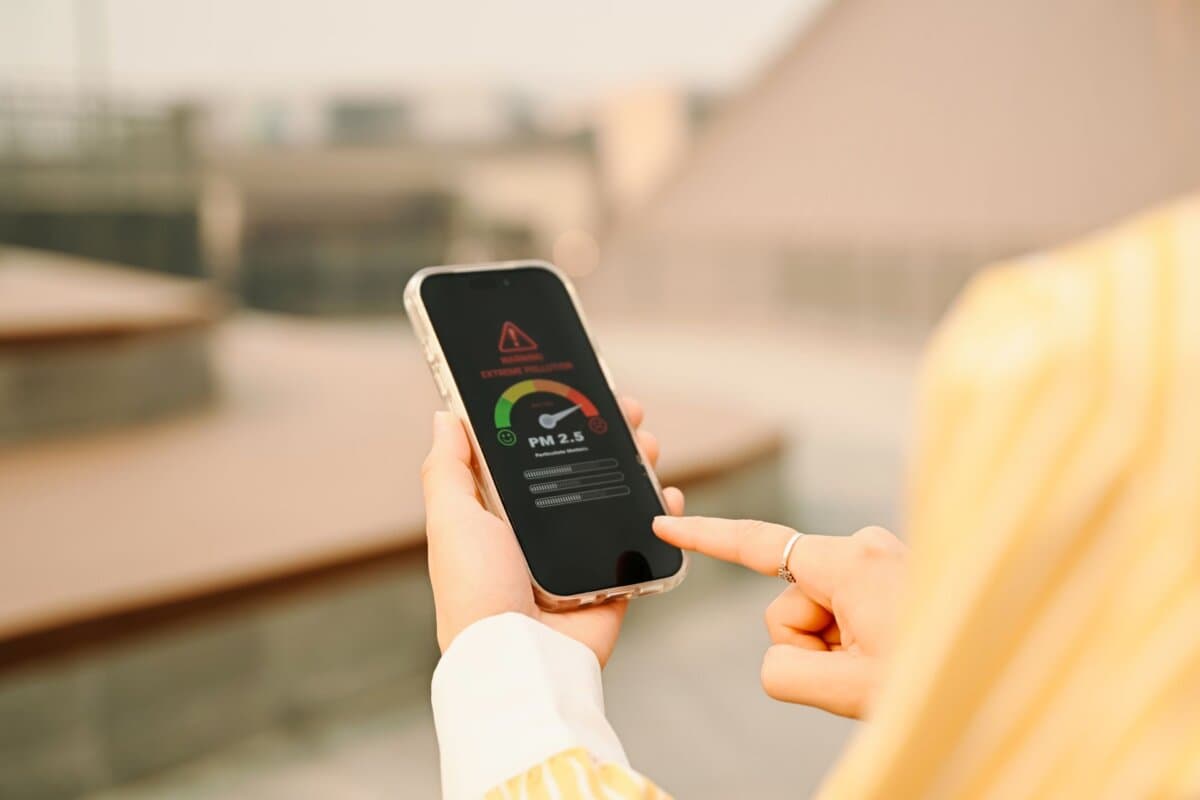 Frau zeigt auf ihrem Smartphone eine PM2,5-Feinstaubwarnung.