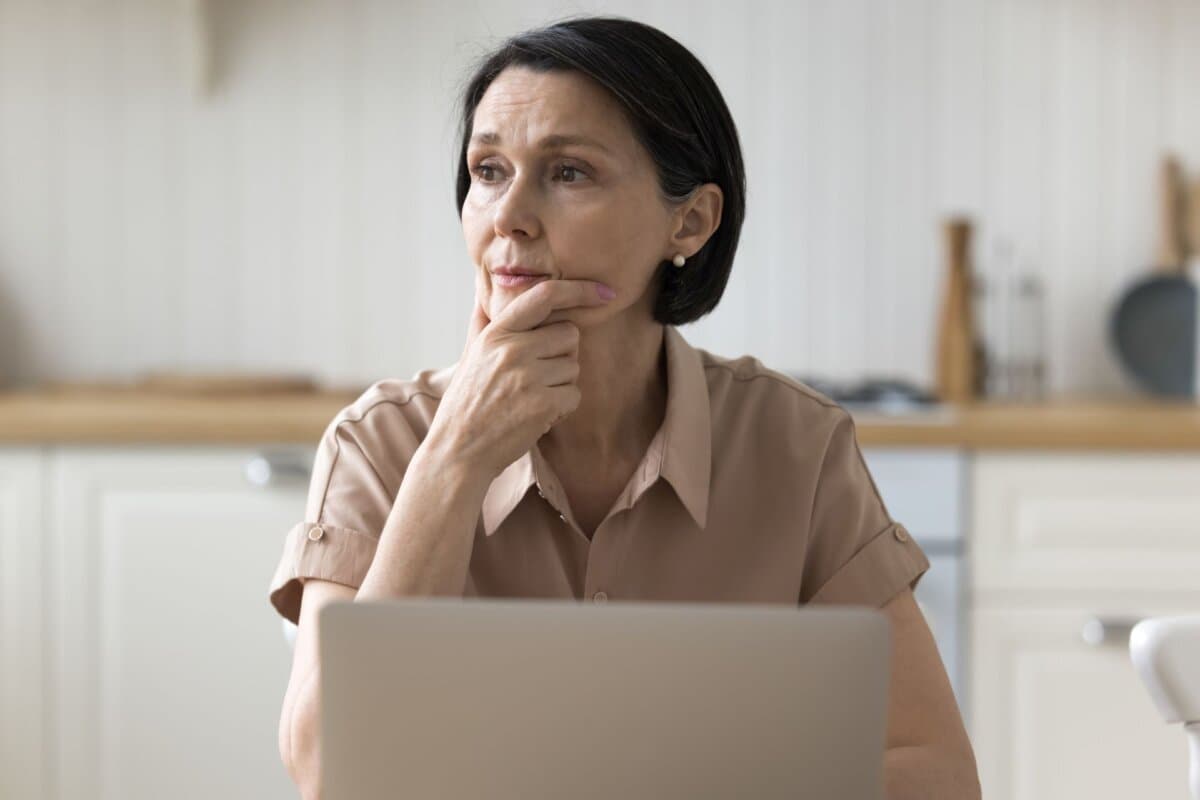 Frau in Gedanken vor dem Laptop.