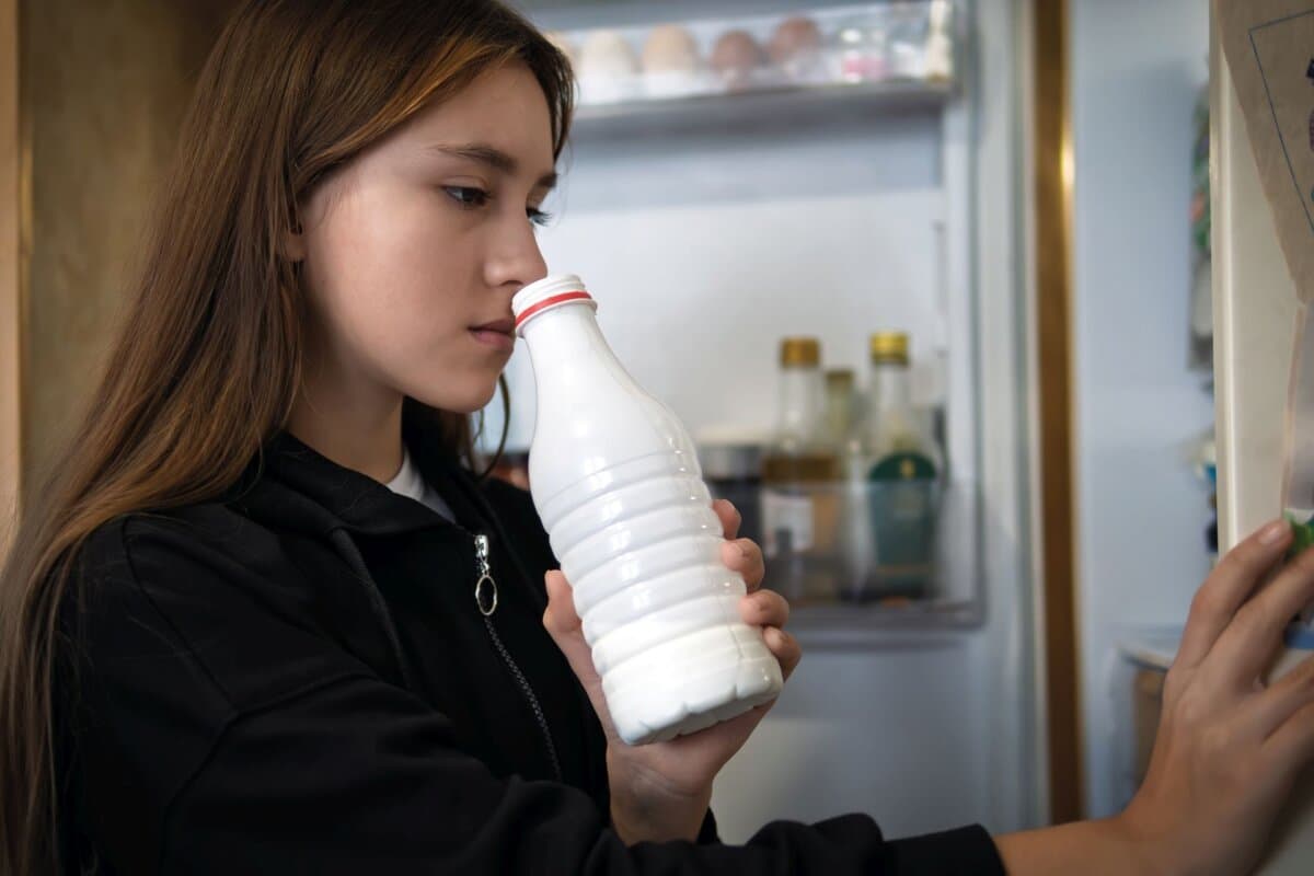 Frau riecht an einer offenen Milchflasche.