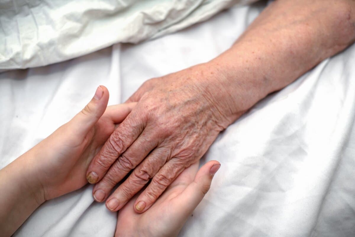 Hände einer jungen Person halten die Hand einer älteren Frau.