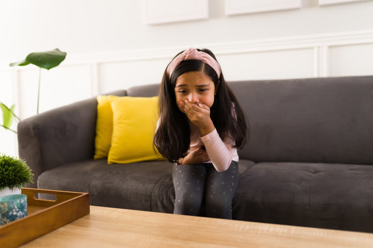 Hispanic girl feels ill and covering her mouth because of the nausea. Little girl suffering from stomach ache wants to vomit