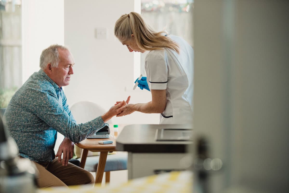 Senior diabetic man is having a check up at home from a district nurse. She is checking his blood glucose levels.