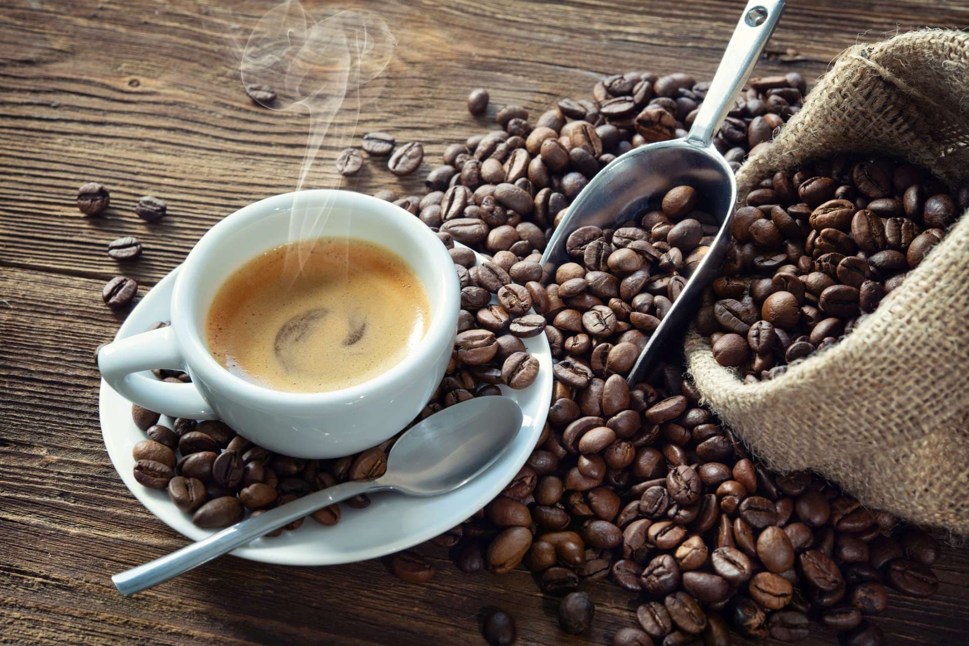 Tasse Espresso mit Kaffeebohnen, Beutel, Schaufel und Dampf auf rustikalem hölzernem Hintergrund