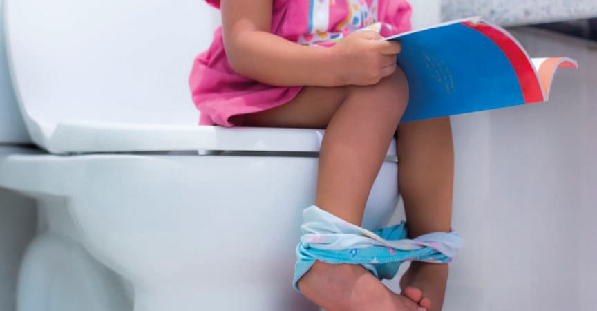 Kleines Kind sitzt auf der Toilette und liest ein Buch.