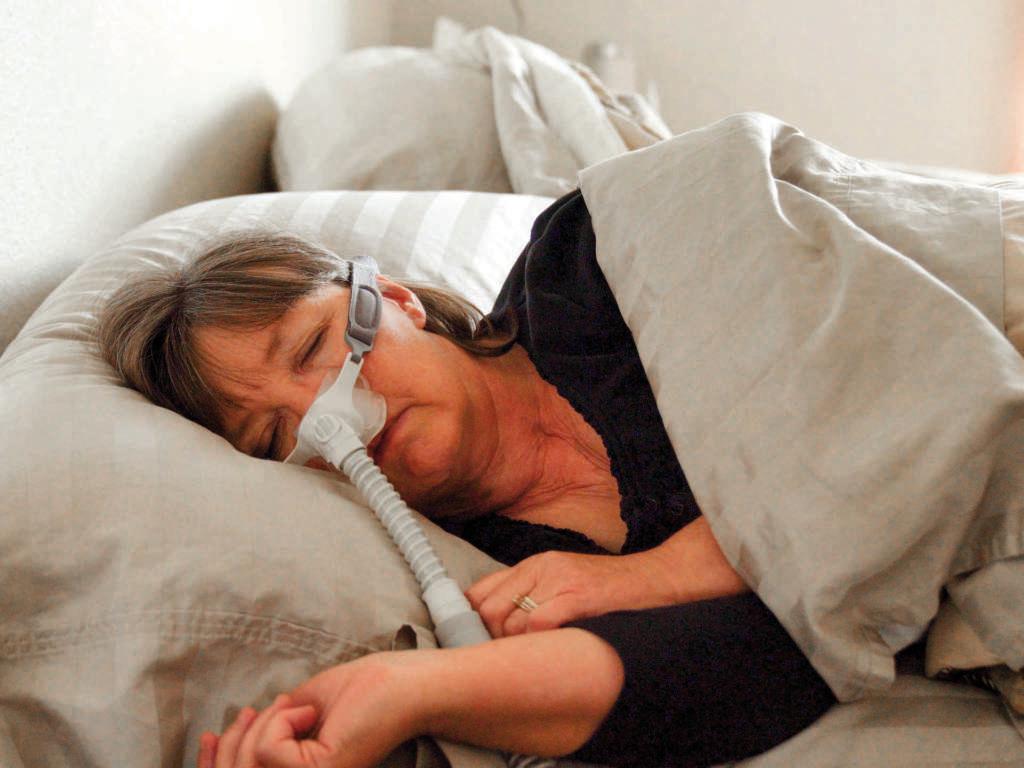 Frau mittleren Alters mit Schlafapnoe, die in einem Bett schläft und ein CPAP-Gerät (Continuous Positive Airway Pressure) trägt, um beim Schlafen zu helfen
