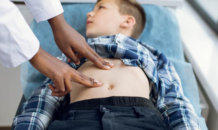 Ein Bub liegt auf einer medizinischen Trage und wird von einer Ärtztin am Abdomen untersucht