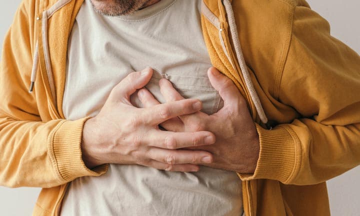 Aching heart and heart attack, adult male with painful grimace pressing the upper abdomen with his hands to ease pain