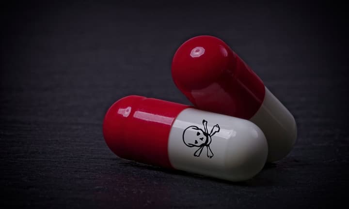 Drug capsules with skull and crossbone on dark stone background.